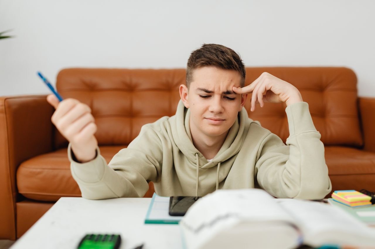 Teen boy concentrating on homework, looking stressed and thoughtful in a cozy indoor setting.